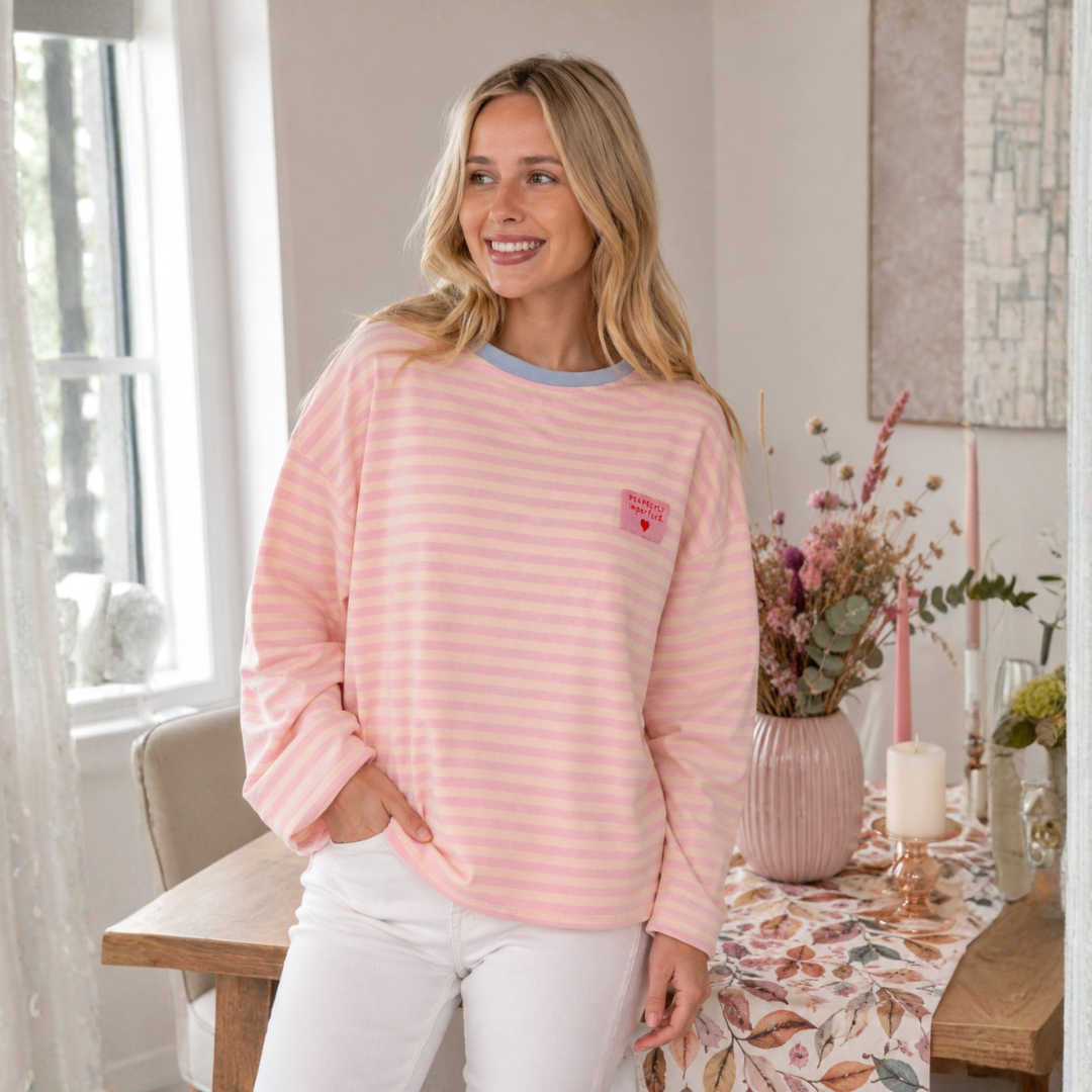 Zwillingsherz Perfectly Imperfect Langarmshirt in Rosa und Creme gestreift mit hellblauem Rundhalsausschnitt und pinkem Herz-Patch.